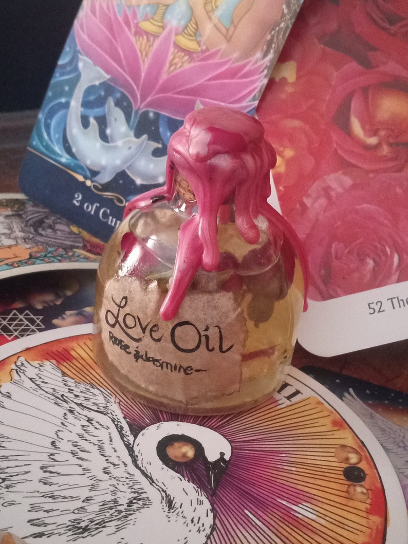 May include: A small glass bottle with a pink wax seal, filled with a clear liquid. The bottle has a label that reads "Love Oil Rose & Jasmine".