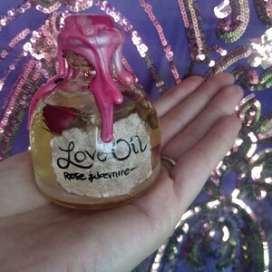 May include: A small glass bottle with a pink wax seal and a label that reads "Love Oil Rose & Jasmine".