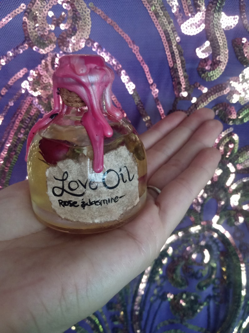 May include: A small glass bottle with a pink wax seal and a label that reads "Love Oil Rose & Jasmine".