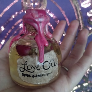 May include: A small glass bottle with a pink wax seal. The bottle contains a clear liquid and has a label that reads "Love Oil Rose & Jasmine".
