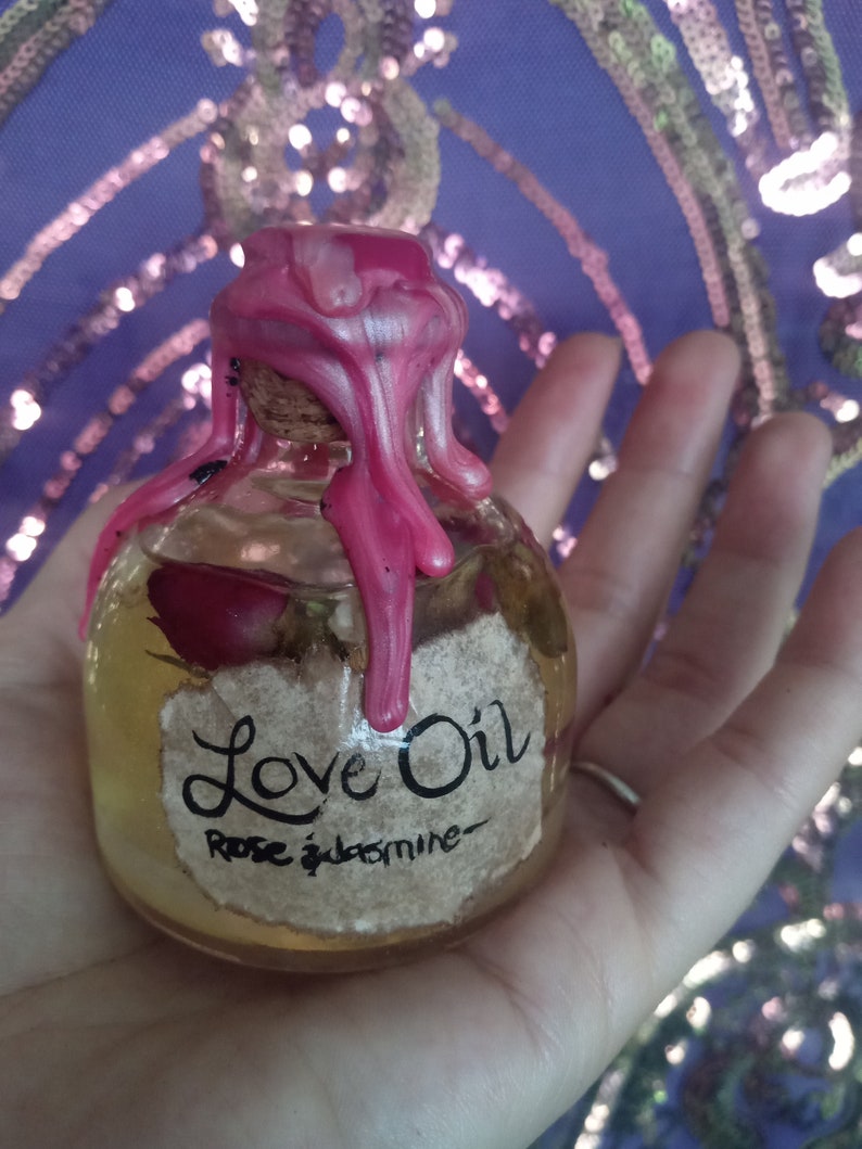 May include: A small glass bottle with a pink wax seal. The bottle contains a clear liquid and has a label that reads "Love Oil Rose & Jasmine".