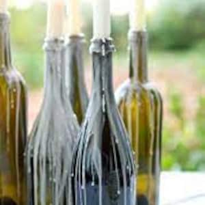 May include: Four glass wine bottles with white candles inside, the wax has dripped down the sides of the bottles, creating a rustic and elegant look.
