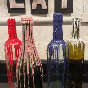 May include: Four glass bottles with different colored wax drippings. The bottles are arranged in a row on a black surface. The bottles are labeled "EAT" in white letters on black signs.