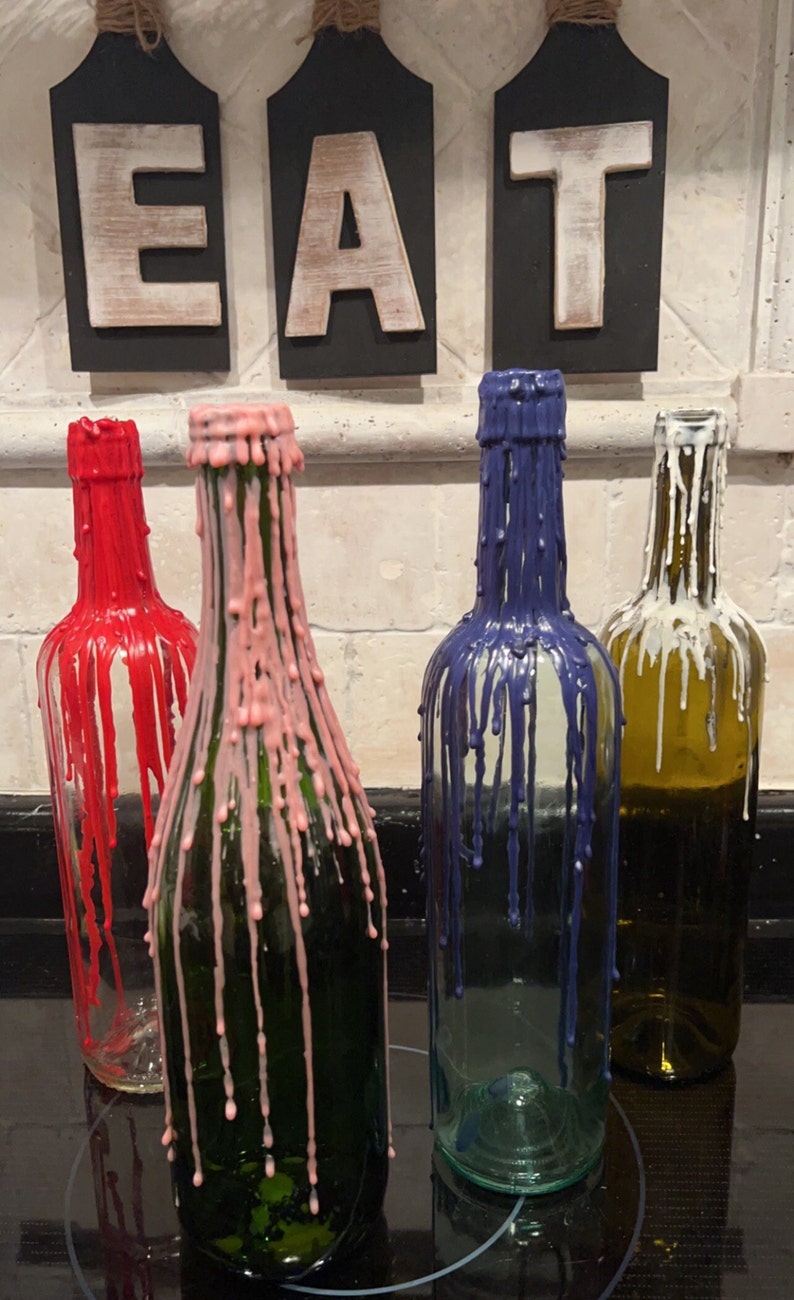 May include: Four glass bottles with different colored wax drippings. The bottles are arranged in a row on a black surface. The bottles are labeled "EAT" in white letters on black signs.