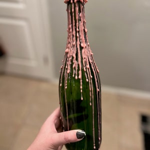 May include: A green glass bottle with pink wax dripping down the sides.