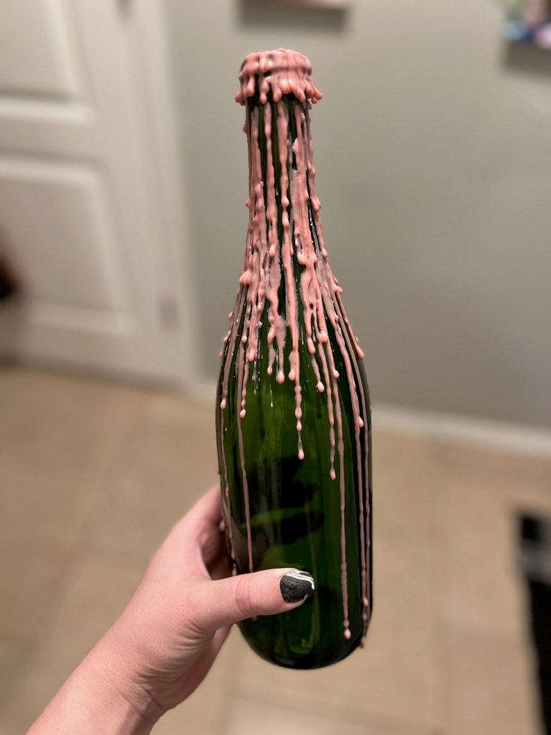 May include: A green glass bottle with pink wax dripping down the sides.