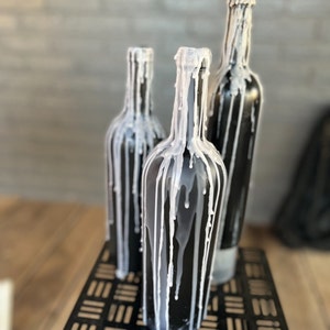 May include: Three black glass bottles with white wax dripping down the sides. The bottles are sitting on a black metal stand.