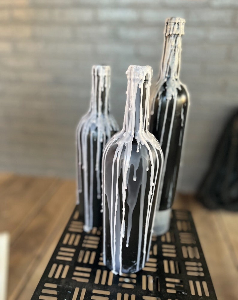 May include: Three black glass bottles with white wax dripping down the sides. The bottles are sitting on a black metal stand.