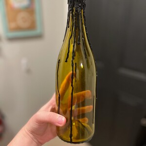 May include: A clear glass bottle with black wax dripping down the sides. The bottle is empty and has a rounded bottom.