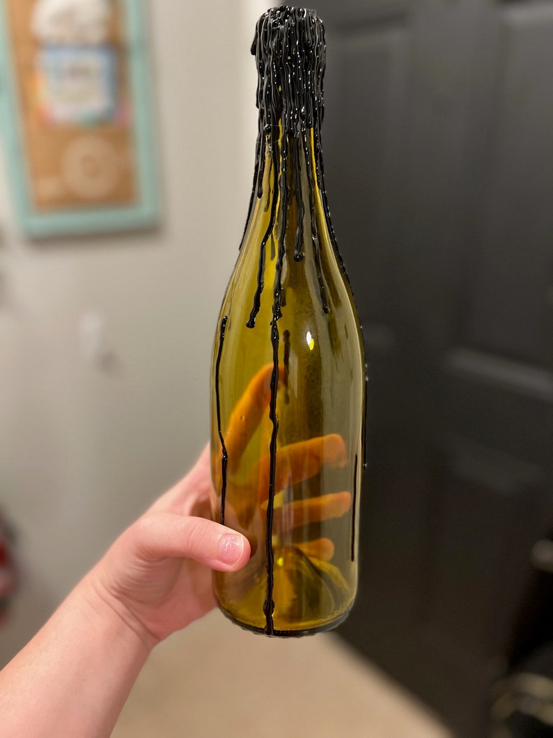 May include: A clear glass bottle with black wax dripping down the sides. The bottle is empty and has a rounded bottom.