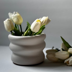May include: White ceramic planter with a wavy design, filled with white tulips.