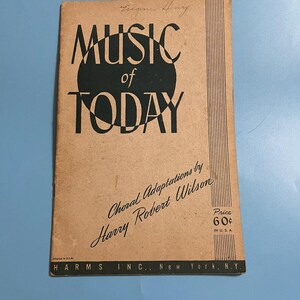 Op de afbeelding: Een vintage muziekboek getiteld "Music of Today" met zwarte tekst op een bruine kaft. De kaft heeft een grote zwarte cirkel met de woorden "MUSIC of TODAY" in vette letters. Het boek is een koorbewerking van Harry Robert Wilson.
