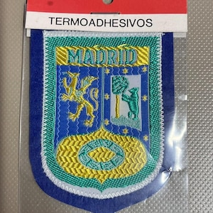 May include: Embroidered Madrid patch with a blue, gold, and green design. The patch features a shield with a lion and a bear, and the word "MADRID". The patch is heat-sealable and comes in a plastic sleeve.
