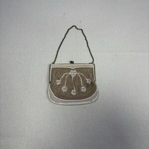 Puede incluir: Un bolso de mano vintage con cuentas y una cadena plateada. El bolso presenta un diseño de cuentas beige y blanco con detalles florales. El borde inferior está adornado con cuentas blancas y el marco es plateado.