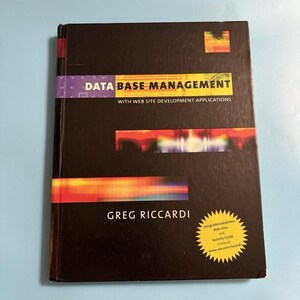 May include: A black hardcover textbook titled Data Base Management with Web Site Development Applications by Greg Riccardi. The cover features abstract orange and red horizontal bars and a yellow starburst sticker with text about online resources.
