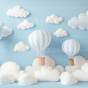 Op de afbeelding: Een blauwe en wit gestreepte luchtballon met een bruine mand, zwevend boven witte, pluche wolken tegen een lichtblauwe achtergrond. Twee andere luchtballonnen zijn zichtbaar op de achtergrond.