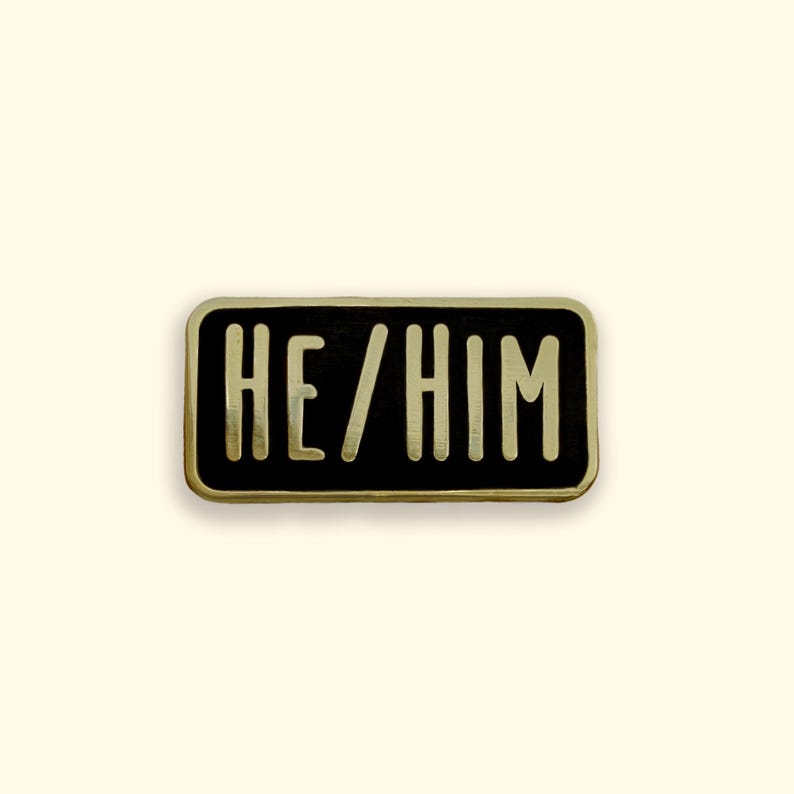 He/Him pronoun black and gold enamel pin badge on yellow background