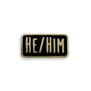 He/Him pronoun black and gold enamel pin badge on white background