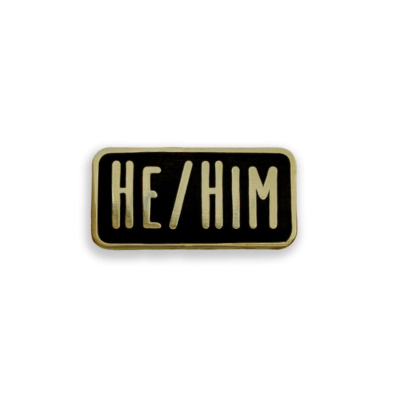 He/Him pronoun black and gold enamel pin badge on white background