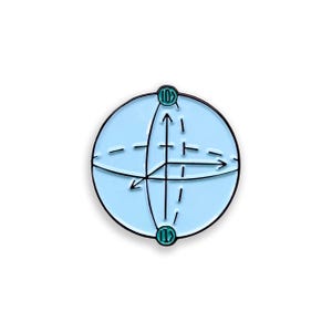 May include: A light blue enamel pin featuring a 3D sphere with intersecting lines and arrows, representing a qubit. The pin has a black outline and teal accents, with the numbers "10>" and "11>" at the top and bottom.