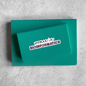 Puede incluir: Un cuaderno de color turquesa con una pegatina que dice "women in bioinformatics".