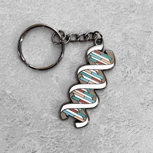 May include: A silver key chain with a white and blue enamel DNA double helix charm. The charm is detailed with red, blue, and brown stripes.