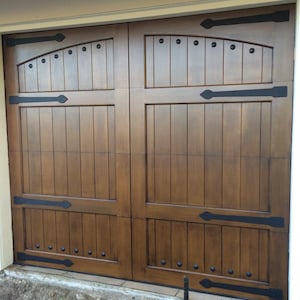 May include: A double wooden garage door with a dark brown stain. The door has a raised panel design with black metal accents and decorative hardware.