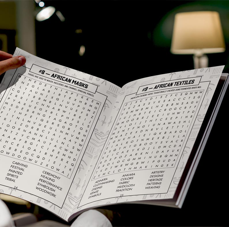 K&ouml;nnte beinhalten: Ein offenes Buch mit den &Uuml;berschriften "#8 - Afrikanische Masken" und "#9 - Afrikanische Textilien." Die Seiten zeigen Wortsuchr&auml;tsel und verwandte Schl&uuml;sselw&ouml;rter wie "Schnitzen", "Farben" und "Weben". Das Buch wird von einer Hand gehalten.