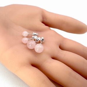 Peut inclure: Deux paires de boucles d'oreilles à clous en quartz rose avec des tiges et des fermoirs en argent. Les boucles d'oreilles présentent des pierres de quartz rose polies, rondes et rose clair. Les boucles d'oreilles sont présentées sur un fond clair.