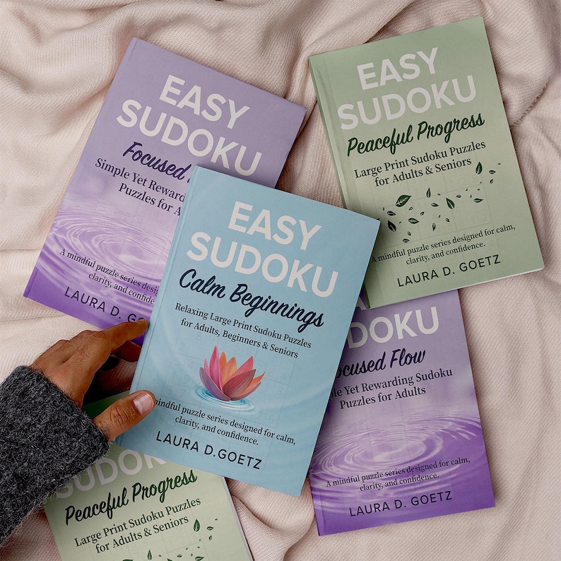 Op de afbeelding: Een verzameling Easy Sudoku puzzelboeken in verschillende kleuren, waaronder lavendel, lichtgroen en blauw. De boeken hebben titels als "Focused", "Calm Beginnings" en "Peaceful Progress". De naam van de auteur, Laura D. Goetz, is op elke omslag zichtbaar.