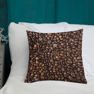 May include: A brown throw pillow with a pattern of coffee beans. The pillow is on a white bed with a teal headboard.