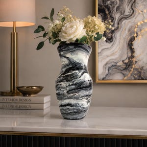 May include: A decorative vase featuring a swirling black and white marbled pattern. The vase has a tapered neck and a rounded body, and it is filled with a bouquet of white flowers, including large peonies and small filler blossoms with green leaves.