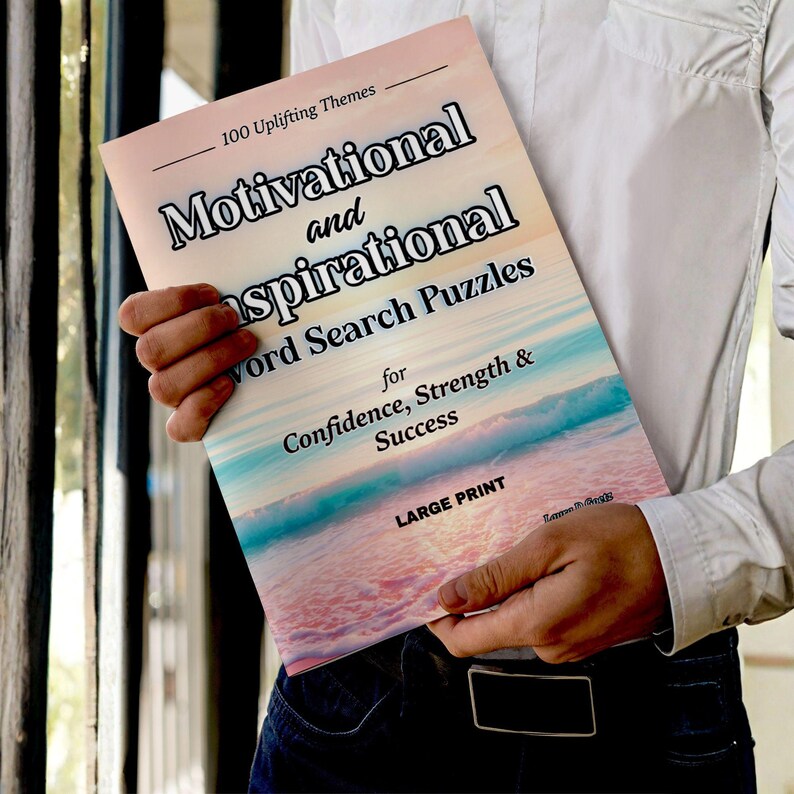 Może przedstawiać: Osoba trzyma książkę zatytułowaną "Motivational and Inspirational Word Search Puzzles". Okładka przedstawia gradient r&oacute;żu, błękitu i bieli z tytułem w kolorze czarnym. Książka opisana jest jako "for Confidence, Strength & Success".