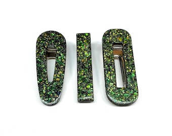 Op de afbeelding: Drie groene glitter haarclips. Twee zijn ovaalvormig en één is rechthoekig. De clips zijn gemaakt van hars en hebben een metallic afwerking.