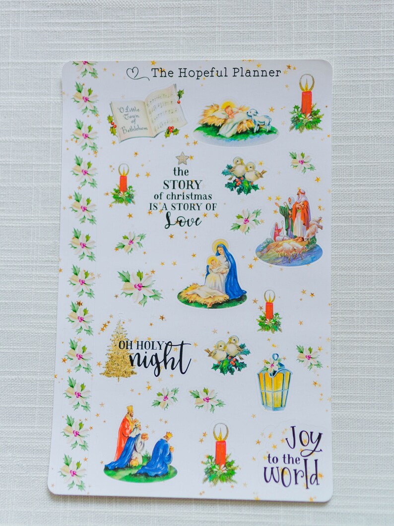 May include: A sheet of Christmas-themed stickers with images of a nativity scene, candles, stars, and the text "the STORY of christmas IS A STORY OF Love", "OH HOLY night", and "Joy to the world".
