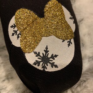 Op de afbeelding: Zwarte instapschoen met een gouden glitterstrik en witte cirkels met zwarte sneeuwvlokontwerpen. De schoen is gemaakt van een textuurstof.