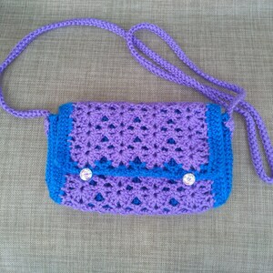 May include: A purple and blue crocheted crossbody bag with a flap closure and two buttons. The bag has a long strap.