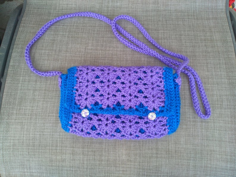 May include: A purple and blue crocheted crossbody bag with a flap closure and two buttons. The bag has a long strap.