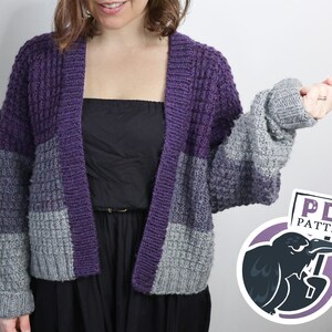 Könnte beinhalten: Ein gestrickter Cardigan in Lila und Grau mit einer strukturierten Maschenart. Der Cardigan ist vorne offen und hat lange Ärmel. Das Bild enthält den Text "PDF PATTERN" mit einem Cartoon-Rabe, der ein Schild hält.