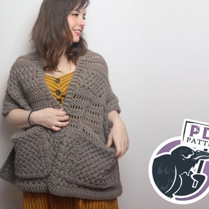May include: A woman wearing a brown crochet shawl with large pockets. The shawl has a lacy pattern and is worn over a yellow striped top. The text "PDF PATTERN" is visible in the image.