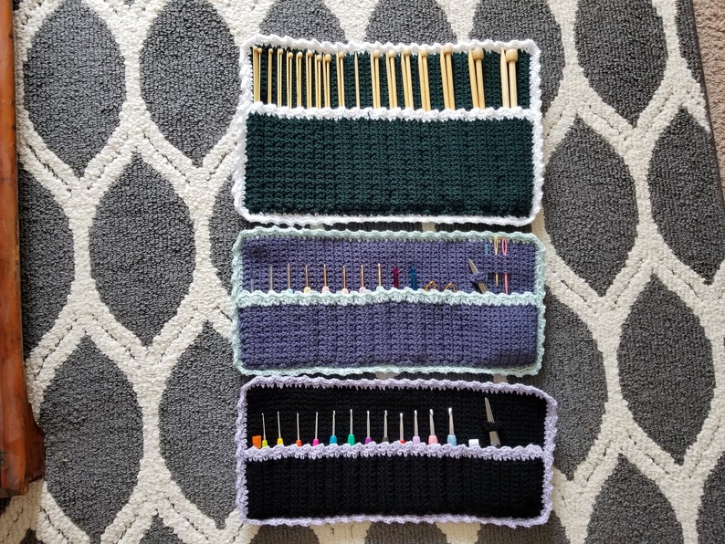 May include: Three crocheted needle holders with different colored fabric and white trim. The top holder is green, the middle is purple, and the bottom is black. Each holder has multiple slots for needles.