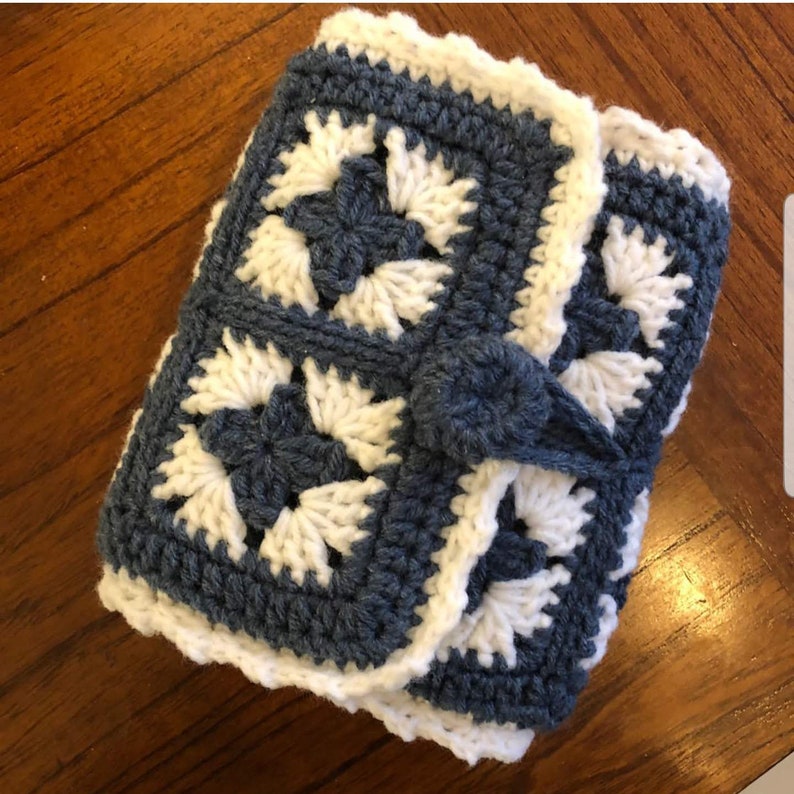 May include: A crocheted clutch purse with a blue and white geometric pattern. The purse has a button closure and a white border.