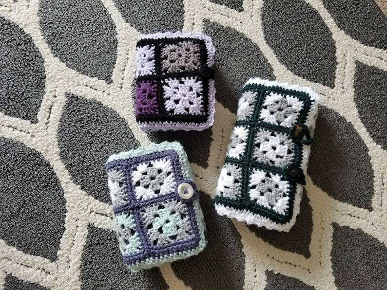 May include: Three crocheted square-shaped pouches in different color combinations. The pouches are made with white, black, gray, purple, and light green yarn. The pouches are on a gray and white patterned rug.