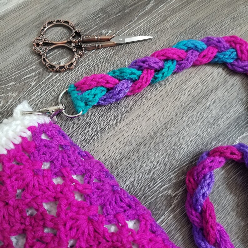 May include: A crocheted bag with a white and pink striped pattern and a braided strap in teal, purple, and pink.