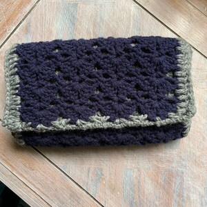May include: A crocheted clutch bag with a dark blue body and a gray border.