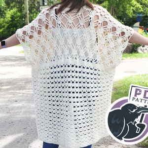 Puede incluir: Un cárdigan de crochet blanco con un diseño de encaje de punto de calado. El cárdigan es largo y tiene un corte holgado. La modelo lleva el cárdigan sobre un top blanco sin mangas y unos vaqueros azules. La imagen también incluye un cartel que dice "PDF PATTERN".