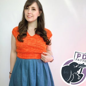 May include: A woman wearing a bright orange knit crop top with a v-neck and short sleeves, paired with a blue denim skirt. The image includes a logo with a black crow holding a sign that says "PDF PATTERN".