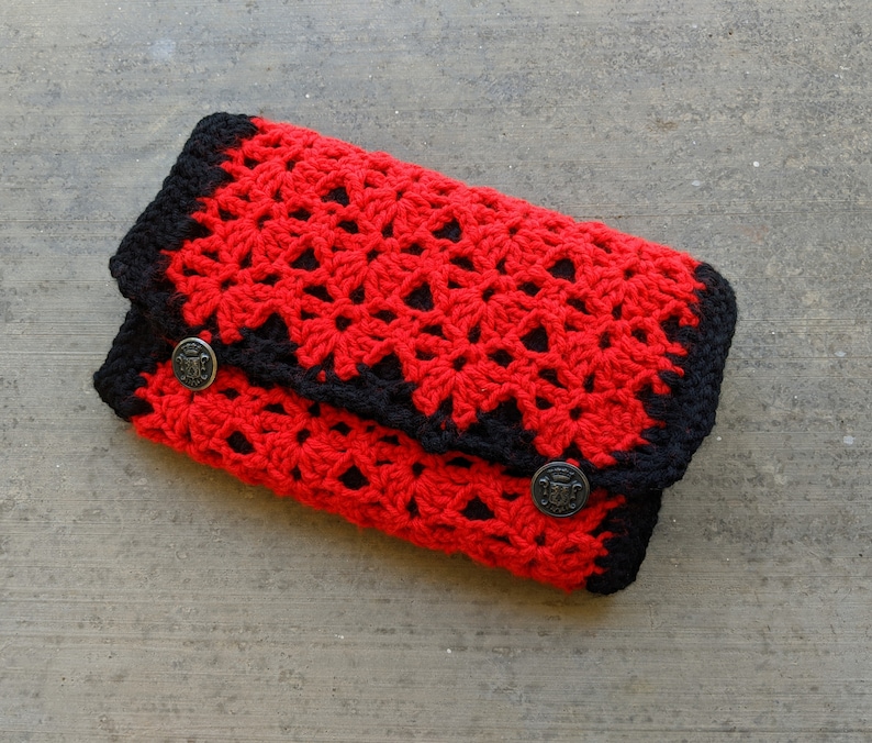 May include: A red and black crocheted clutch with two decorative buttons.