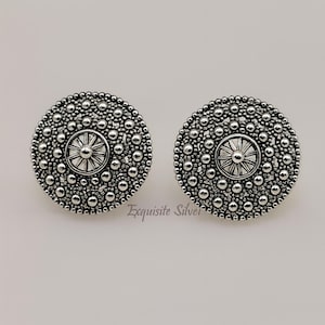 Könnte beinhalten: Ein Paar silberfarbene Ohrstecker. Jeder Ohrring hat ein kreisförmiges Design mit einem zentralen Sonnenstrahlmuster, das von kleinen, erhabenen Perlen umgeben ist. Der Text "Exquisite Silver" befindet sich unten.