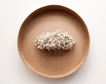 May include: A white dried flower hair comb on a brown cardboard background.